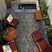An outdoor patio scene features Couristan Dolce Indoor/Outdoor Rug - Mala/Smoke beneath wooden furniture and near a koi pond