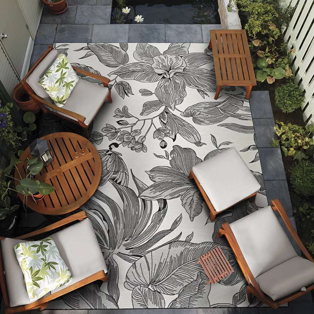 An outdoor patio setup features Couristan Dolce Indoor/Outdoor Rug - Flora/Snow centered among wooden lounge chairs and potted plants