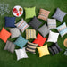 An assortment of colorful LuxCraft 19 Throw Pillows in various solid and striped patterns is spread across a grassy lawn