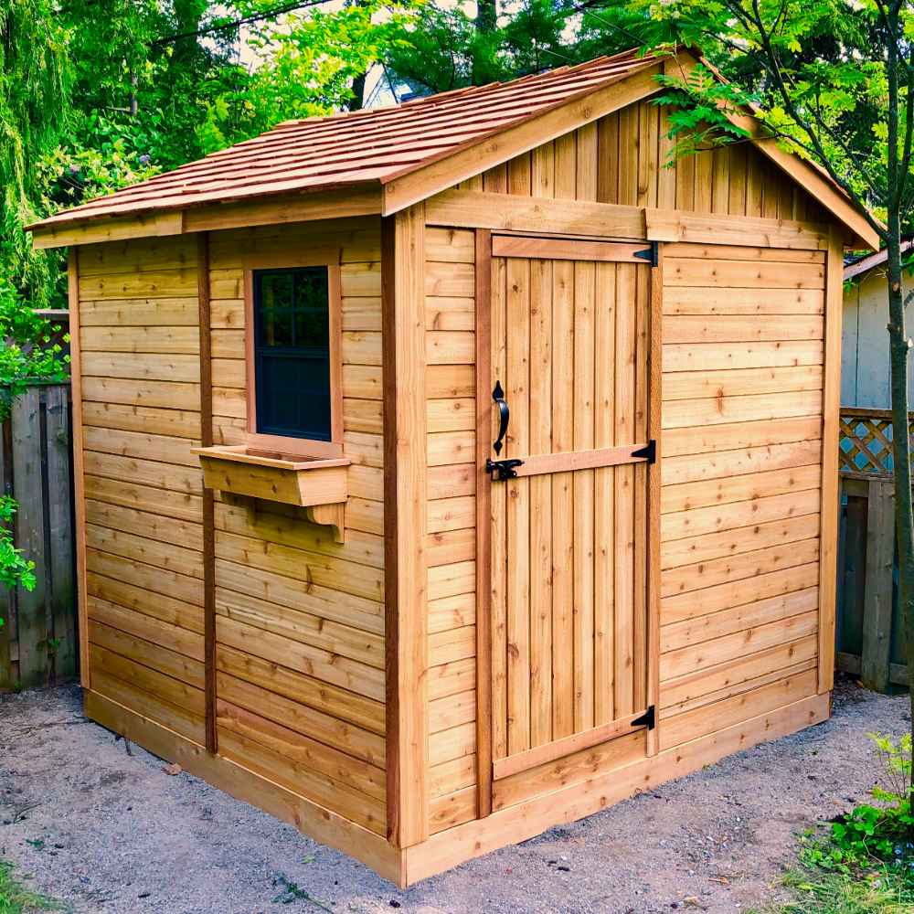 A natural wood shed with a front door, side window, and flower box, surrounded by trees, highlighting the Outdoor Living Today 8×8 Gardener Shed