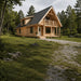 Two-story light wood cabin with a black metal gabled roof, balcony, and porch, set in a green forest clearing.
