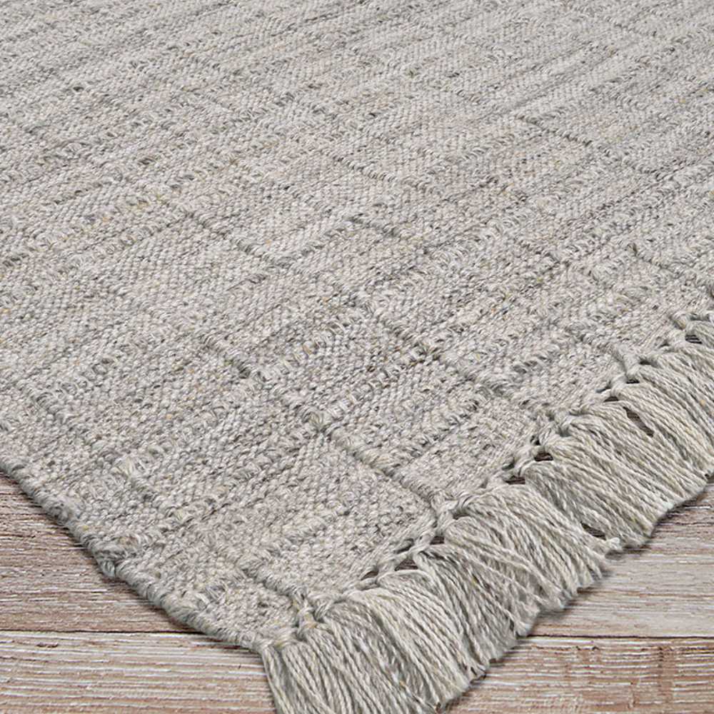 Angled view of the Couristan Ascot Indoor/Outdoor Rug - Windowpane/Linen highlights the clean grid texture and fringed border on a deck-style floor