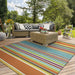 An outdoor patio setting features the Couristan Covington Indoor/Outdoor Rug - Sherbet Stripe/Multi adding a burst of color beneath wicker furniture on a wooden deck
