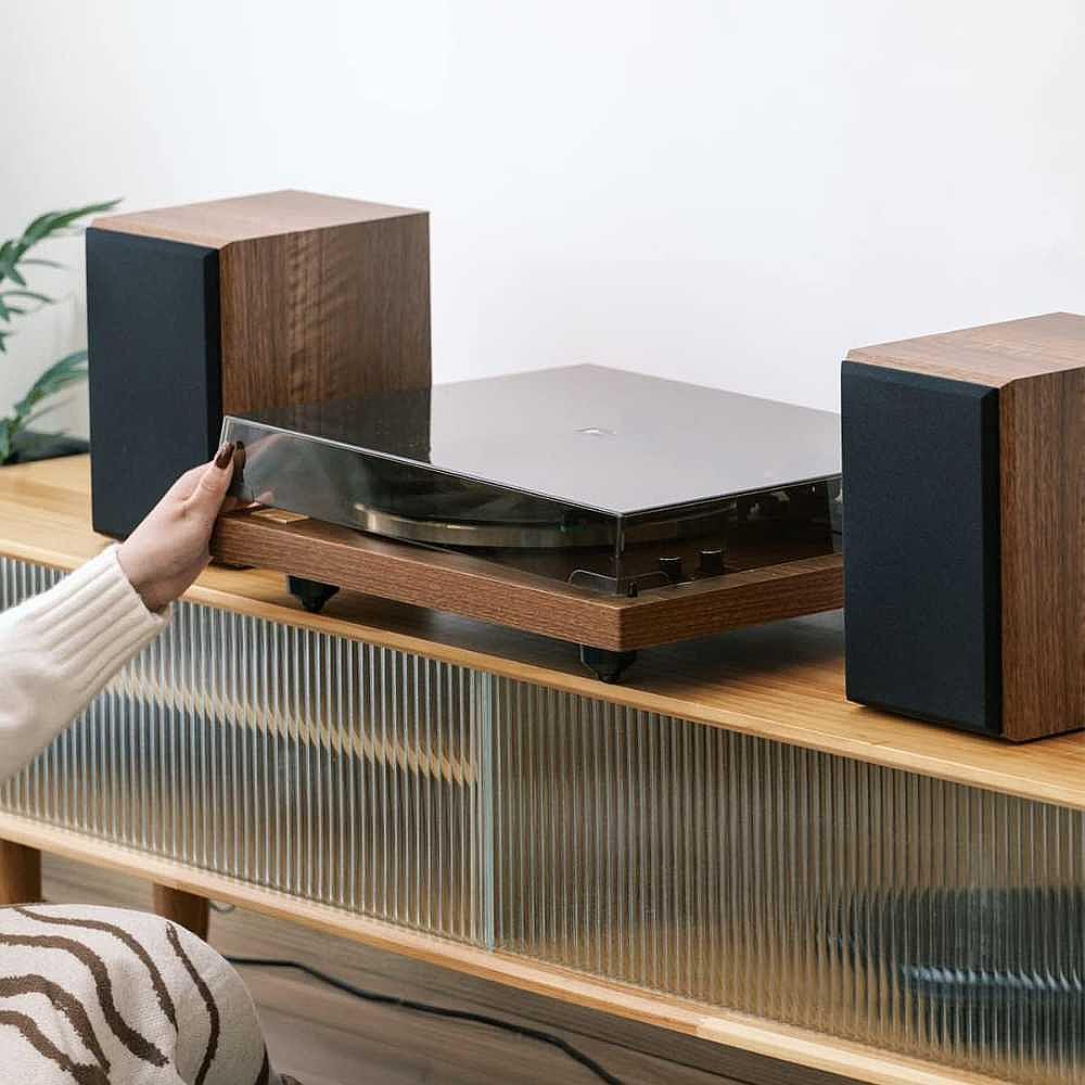 A person is gently lifting the dust cover of Arkrocket Cassini Bluetooth Vinyl Turntable Record Player 40 Watt Stereo Bookshelf Speakers