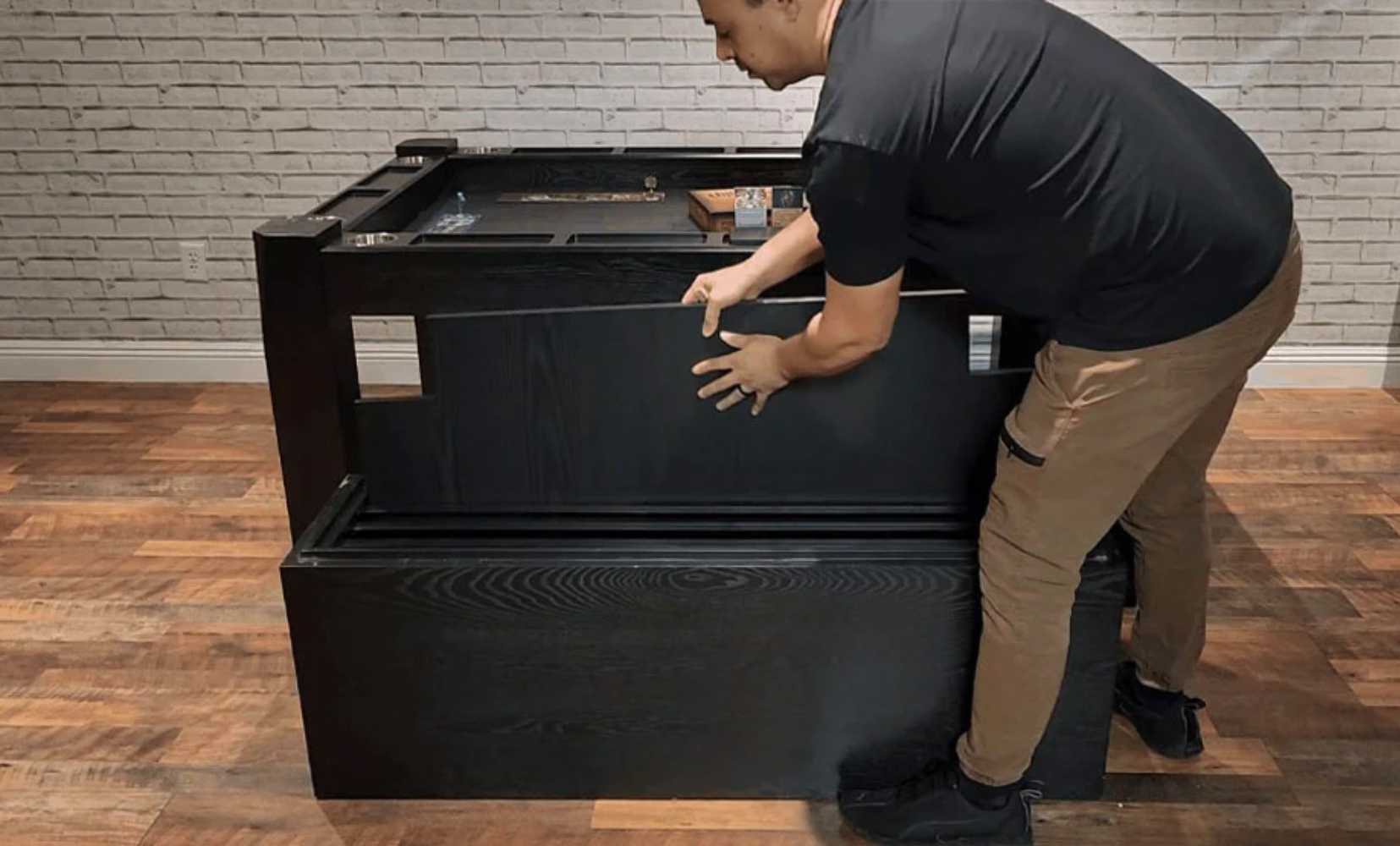 A person is lifting the lid of a Game Theory Tables Bench For Origins Game Table, revealing its storage space