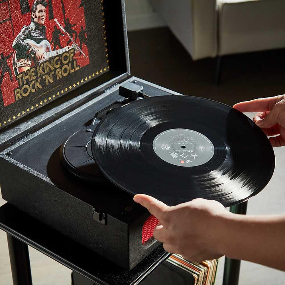 A person is placing a vinyl record on the Arkrocket x Elvis Bluetooth Portable Record Player - Elvis Presley '68 turntable