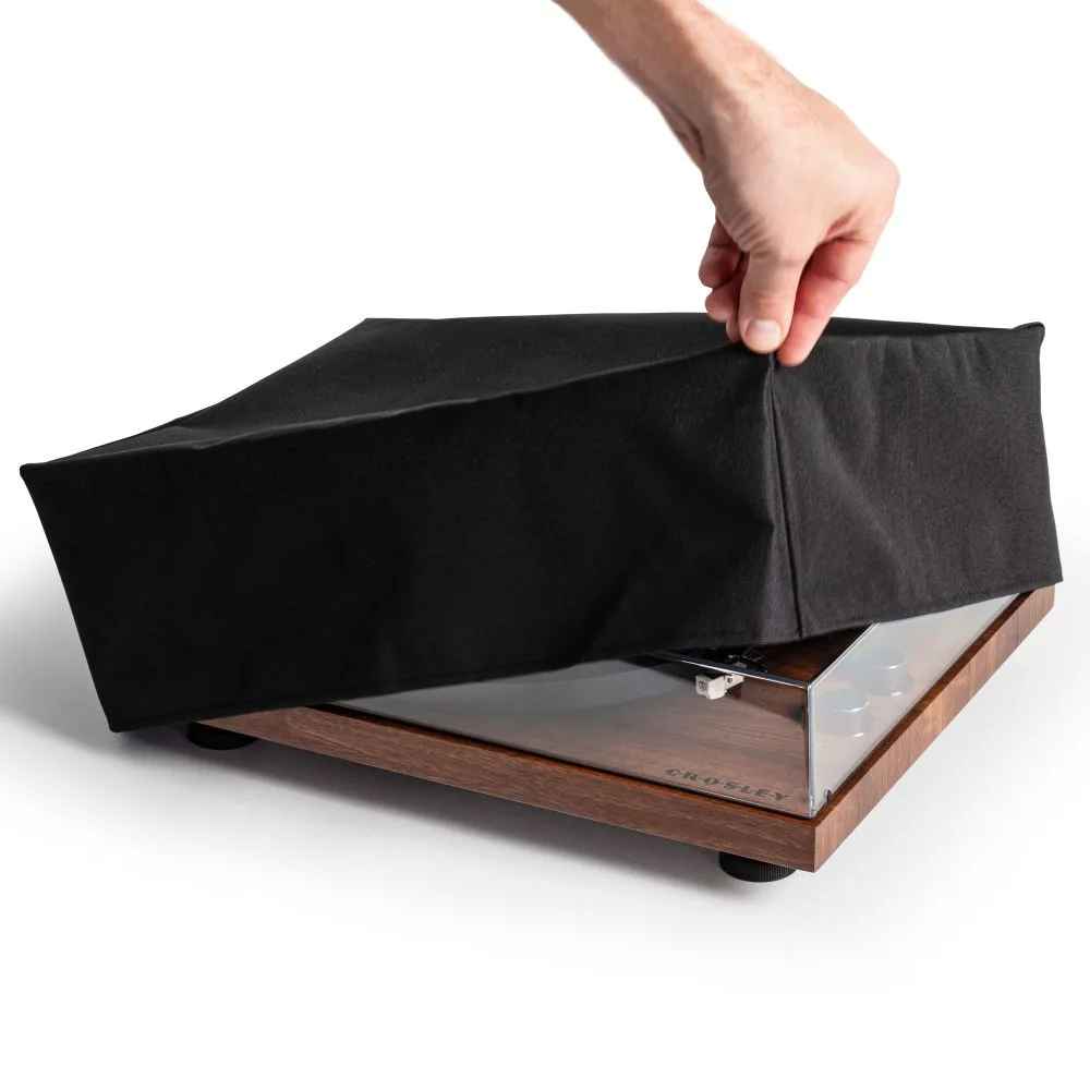 A person lifts the Crosley Fabric Turntable Dust Cover - Black to reveal a wooden turntable underneath