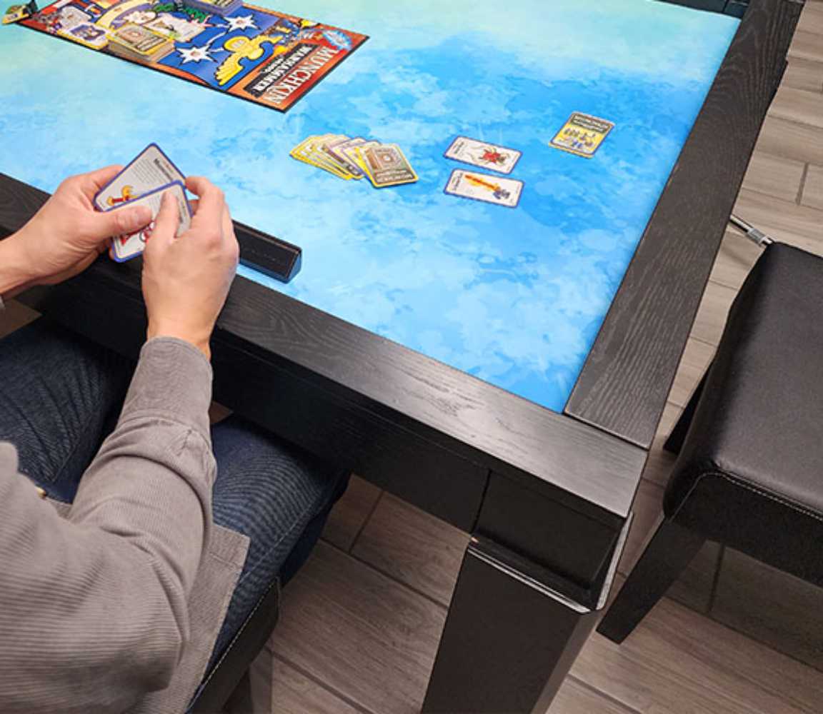 A person plays a card game on the Game Theory Tables The Meeples Champion Game Table with a vivid blue surface