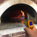 A person using the Chicago Brick Oven Infrared Thermometer Gun to measure the temperature inside a wood-fired oven