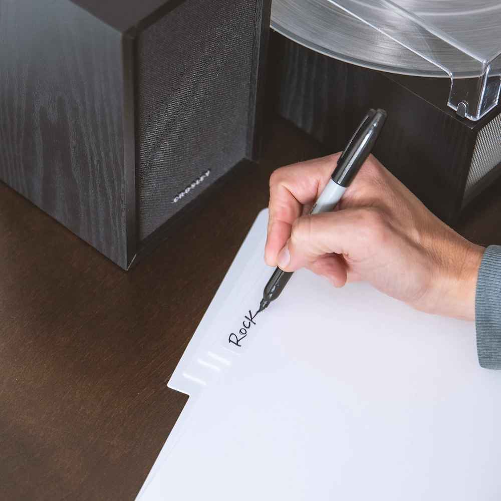 A person writes Rock on a white tabbed divider with a black marker, demonstrating customization with Crosley Vinyl Record Dividers - White