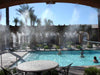A resort pool area with guests in and out of the water stays cool thanks to the Aeromist Pinnacle 1000 PSI Misting System spraying mist along the shaded pergola