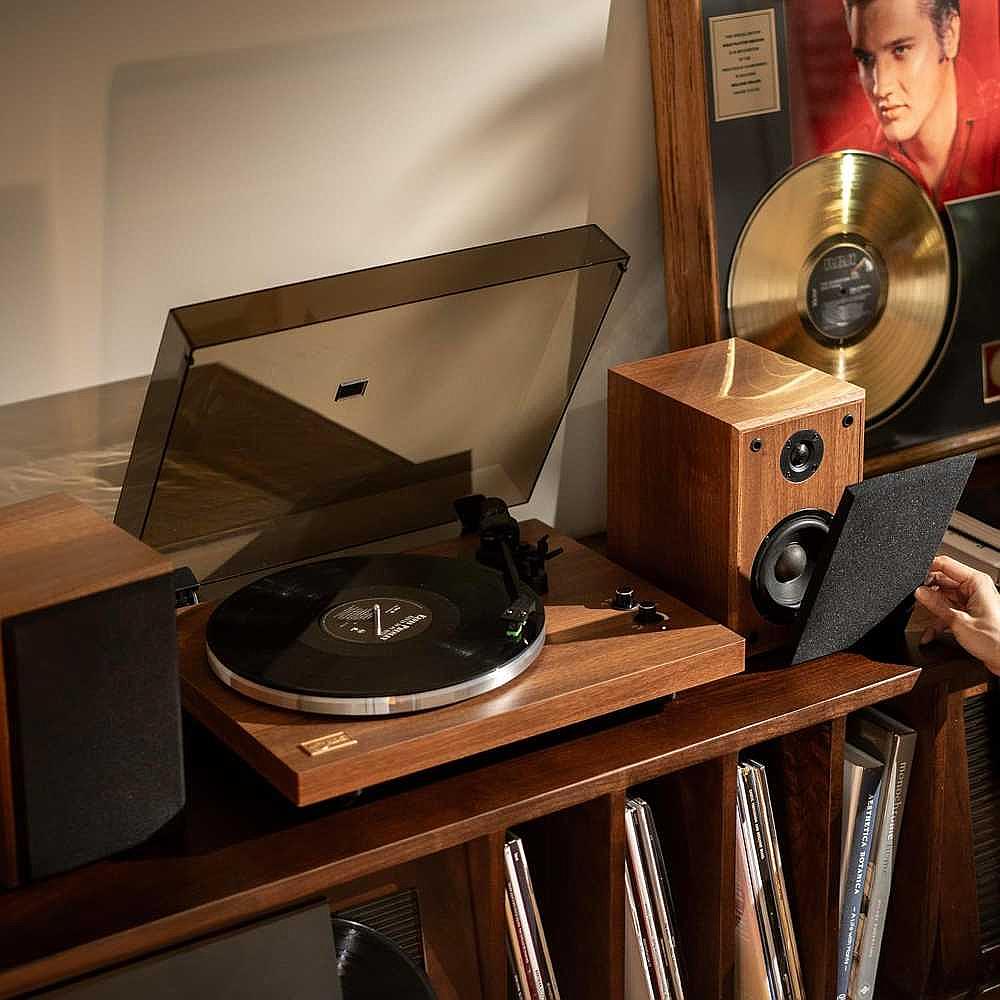 Arkrocket Cassini Bluetooth Vinyl Turntable Record Player 40 Watt Stereo Bookshelf Speakers is displayed in a cozy room setting with records and a gold record on the wall