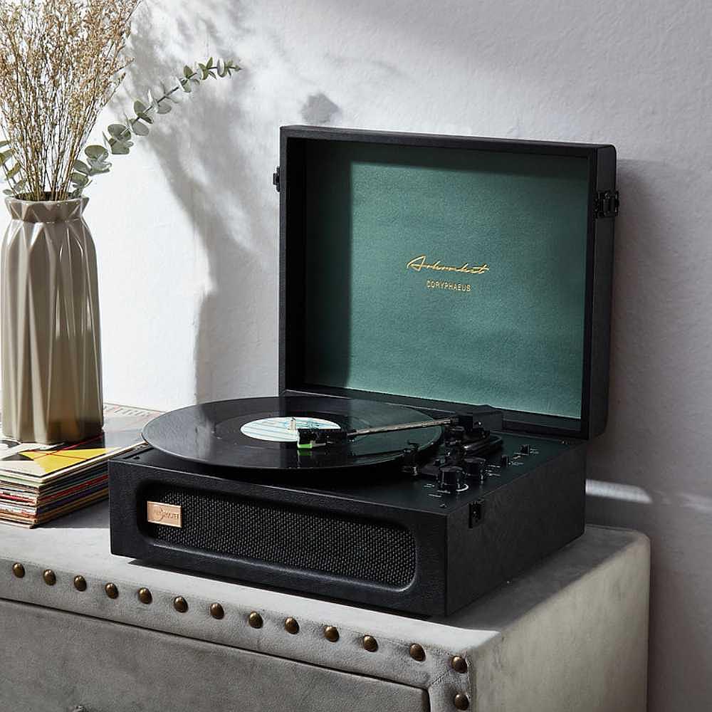 Arkrocket Coryphaeus Bluetooth Record Player with Record Storage Case (BlackGreen) is displayed on a table with a vinyl record playing and a decorative vase next to it