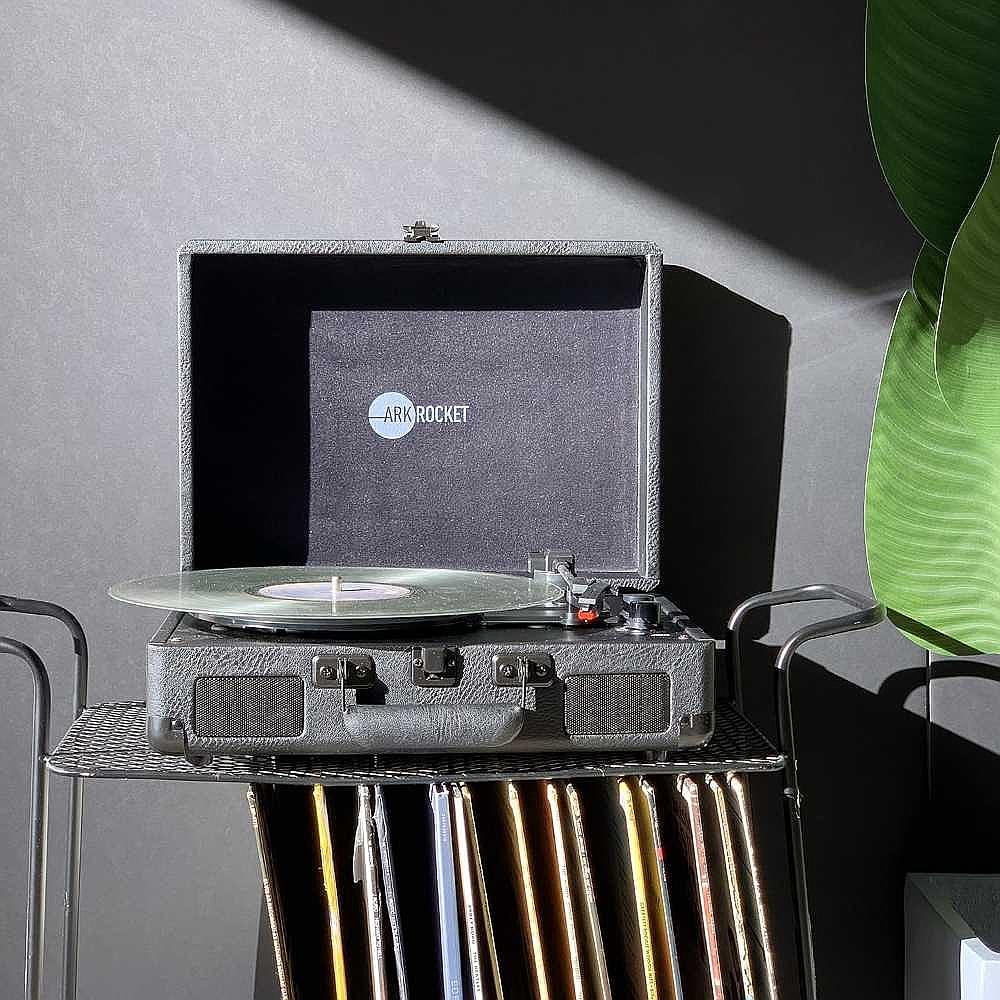 Arkrocket Curiosity Suitcase Bluetooth Turntable (Black), open with a vinyl record spinning on the turntable, set against a dark background with a plant in view