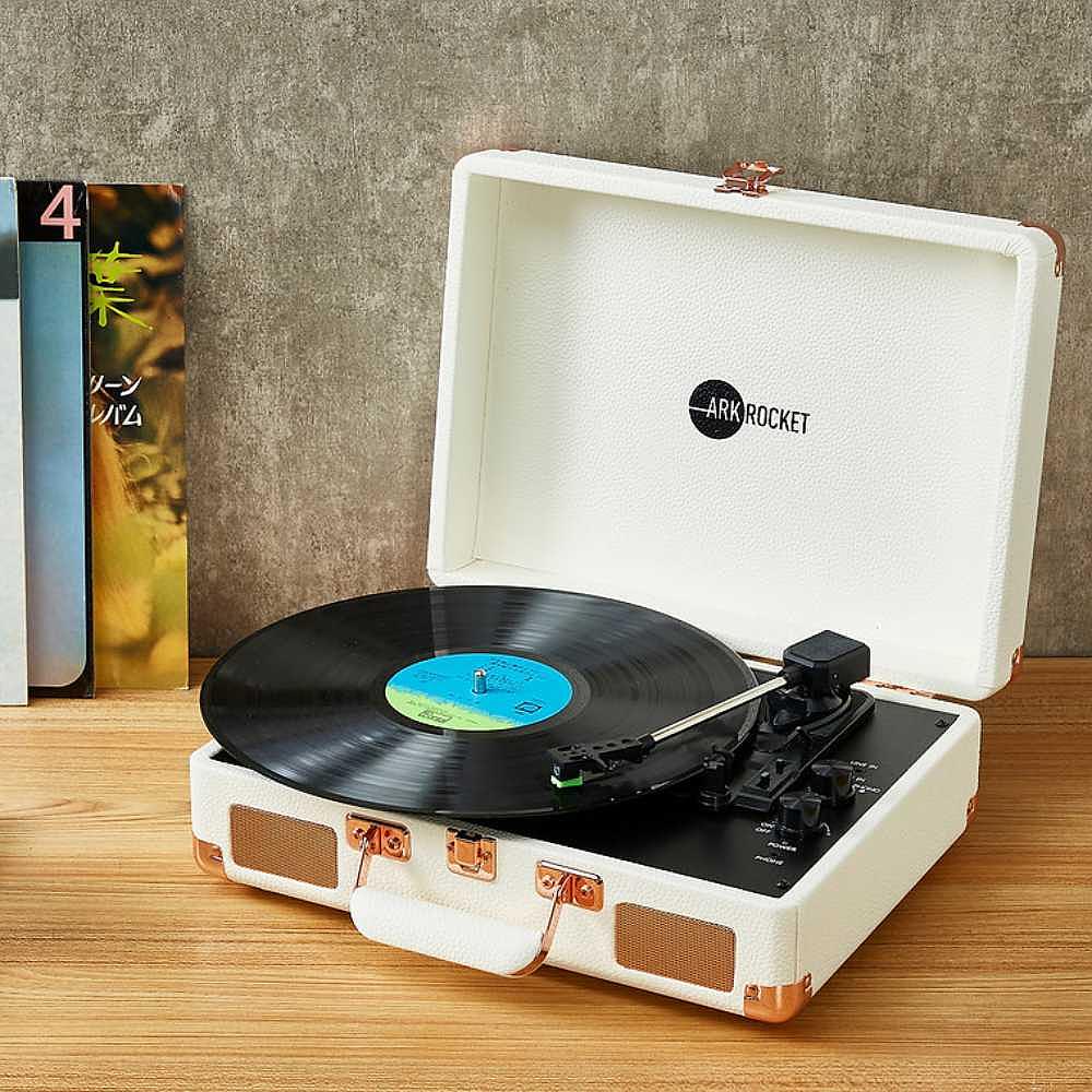 Arkrocket Curiosity Suitcase Bluetooth Turntable (Cream Rose Gold) with an open case and a record playing on it, placed on a wooden surface next to vinyl records