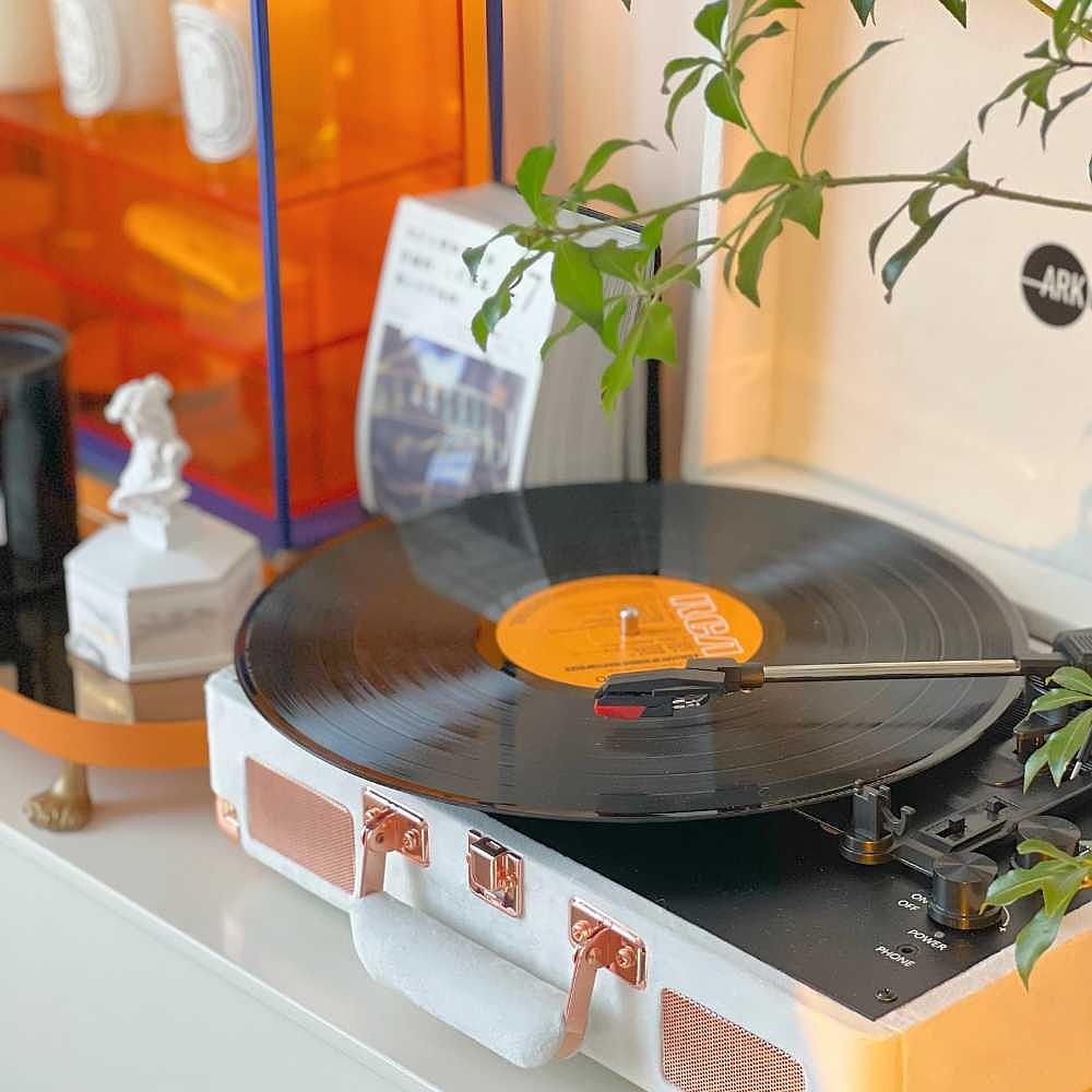 Arkrocket Curiosity Suitcase Bluetooth Turntable (Cream Velvet) is displayed on a table with books and plants around