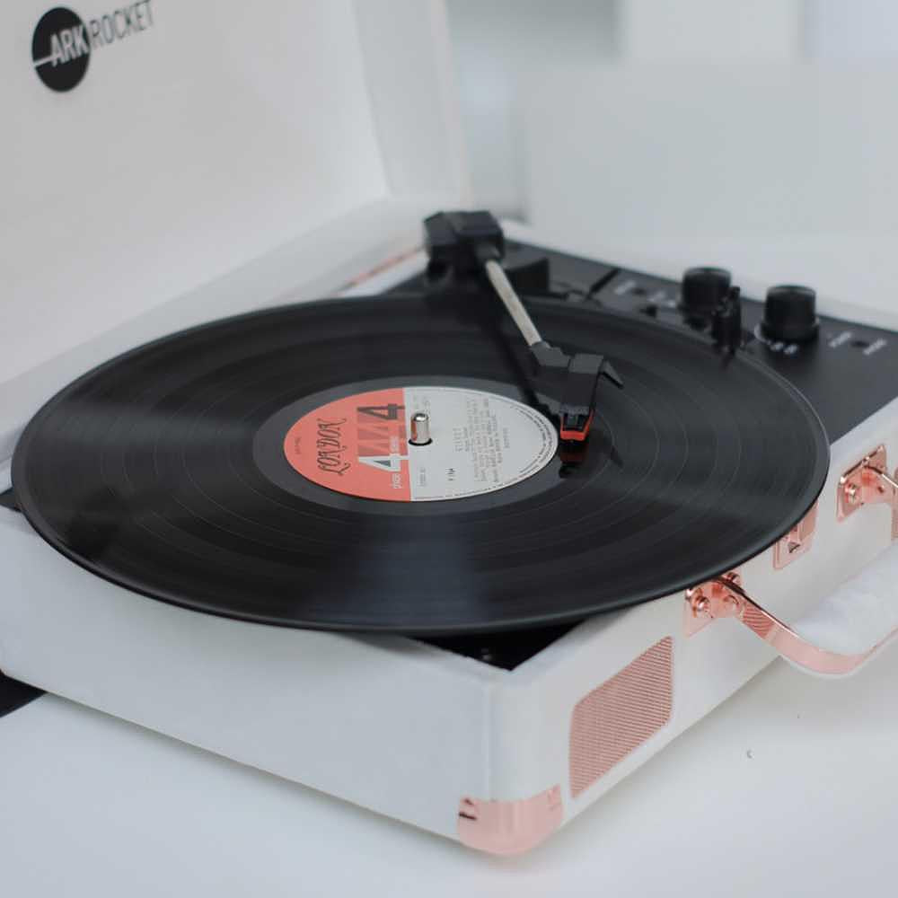 Arkrocket Curiosity Suitcase Bluetooth Turntable (Cream Velvet) is shown playing a black record with a red label