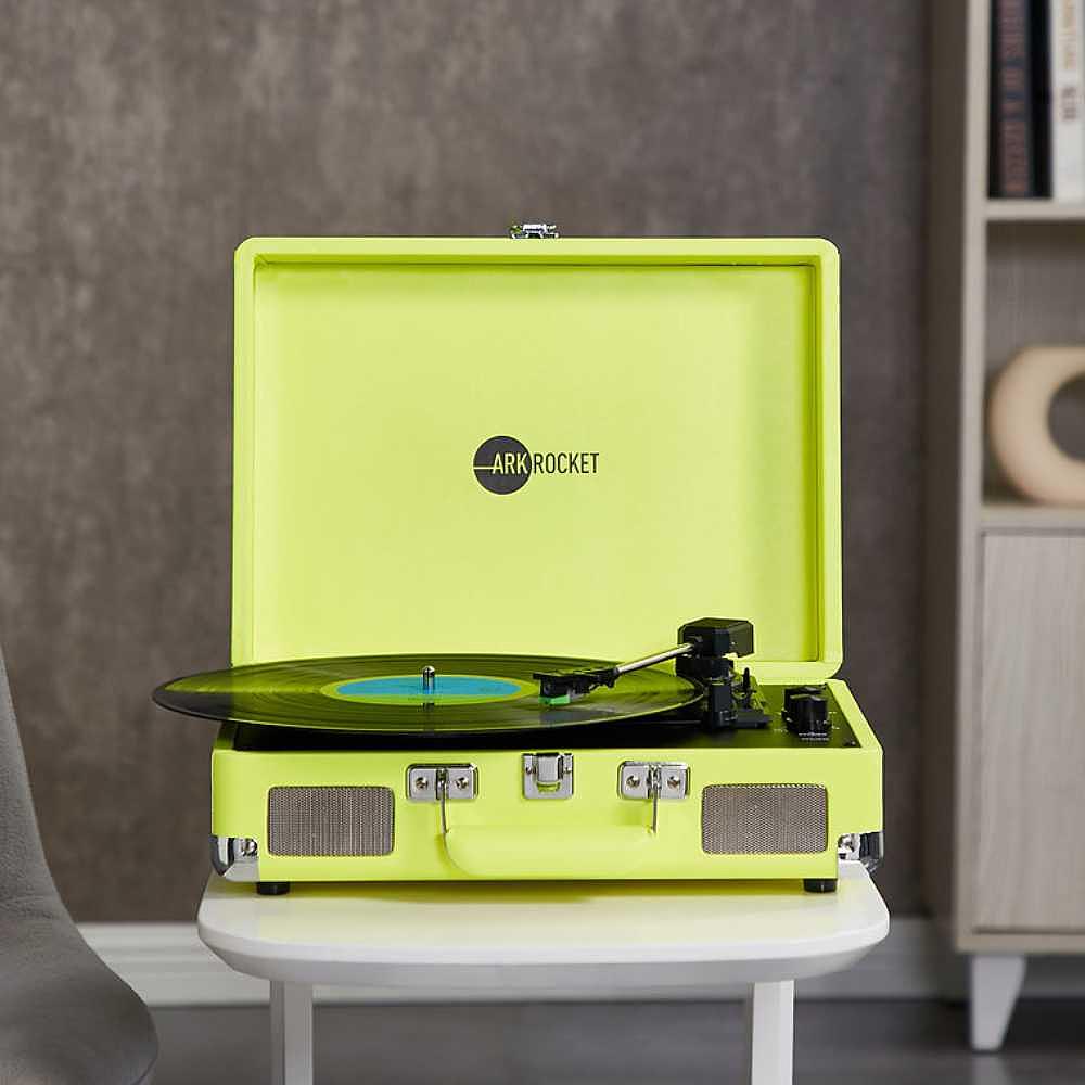 Arkrocket Curiosity Suitcase Bluetooth Turntable (Neon Yellow) is placed on a white table playing a record with its lid open