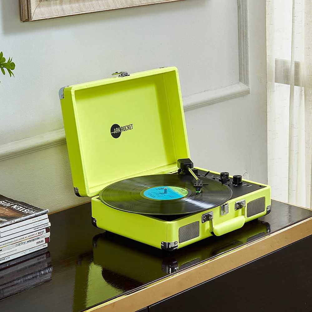 Arkrocket Curiosity Suitcase Bluetooth Turntable (Neon Yellow) is playing a record on a wooden cabinet