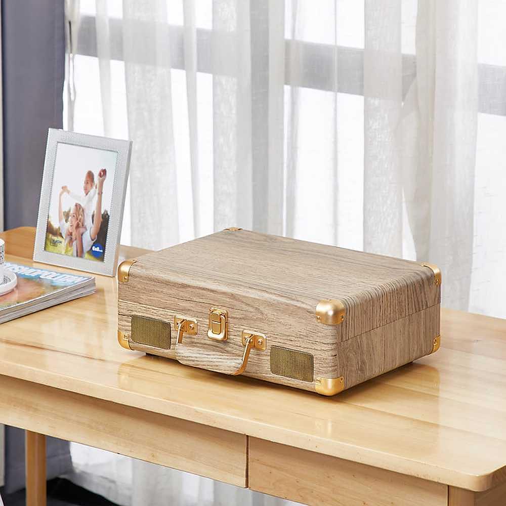 Arkrocket Curiosity Suitcase Bluetooth Turntable (Wood Grain) is closed with its suitcase design displayed on a wooden surface