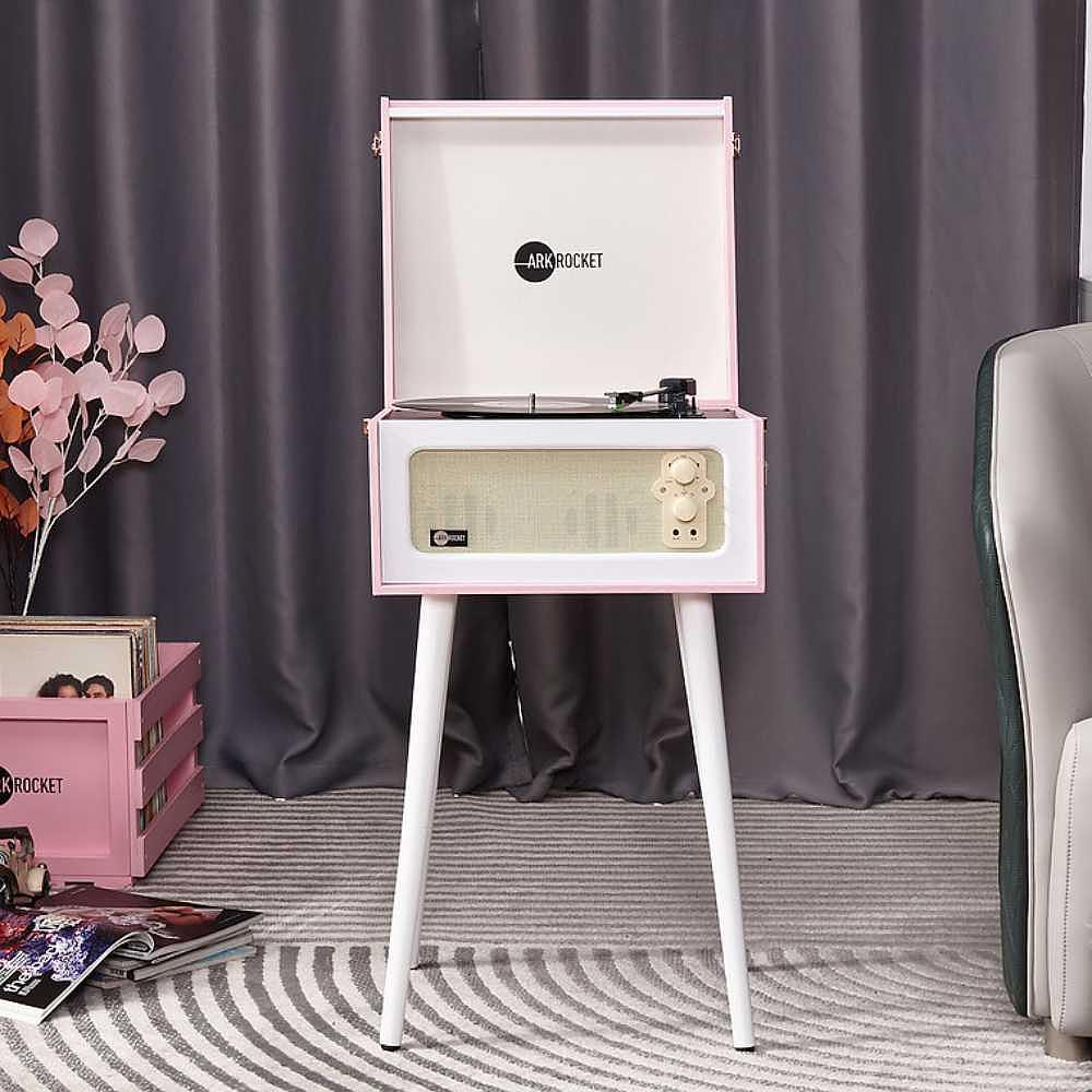 Arkrocket Discovery Bluetooth Record Player Stand with 3-Speed Turntable (PinkWhite) is set up in a cozy living room against a gray curtain