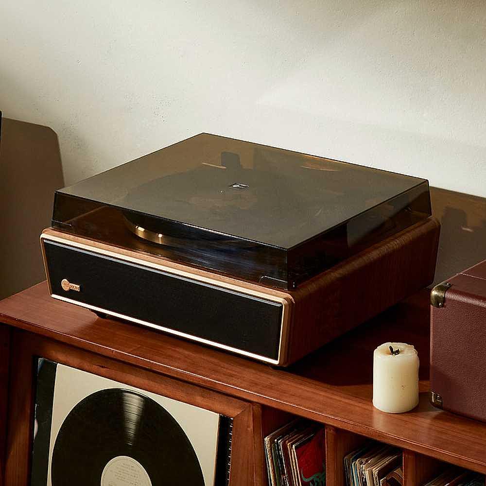 Arkrocket Huygens Bluetooth Turntable with Built-in Speakers (Walnut) with the dust cover closed resting on a wooden cabinet filled with records