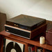 Arkrocket Huygens Bluetooth Turntable with Built-in Speakers (Walnut) with the dust cover closed resting on a wooden cabinet filled with records