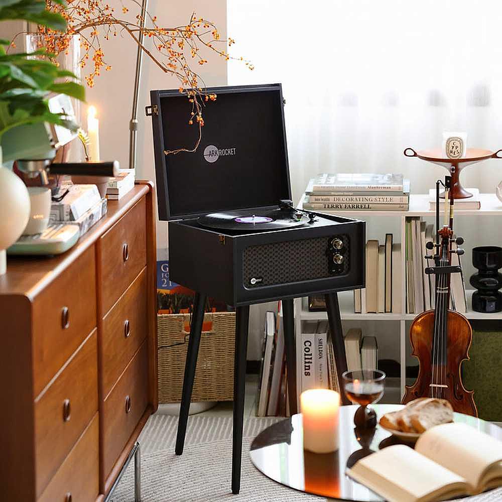 Arkrocket Retro Turntable Wireless Record Player With Legs (Black) is shown as part of a room setting with soft lighting and a violin on display