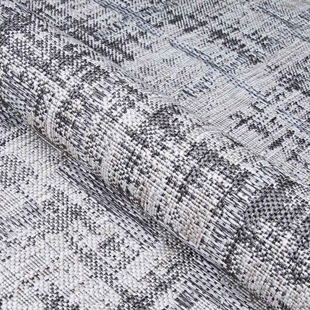 A rolled edge of the Couristan Charm Indoor/Outdoor Rug - Tiverton/Anthracite-Light Grey reveals its flexibility and fine texture