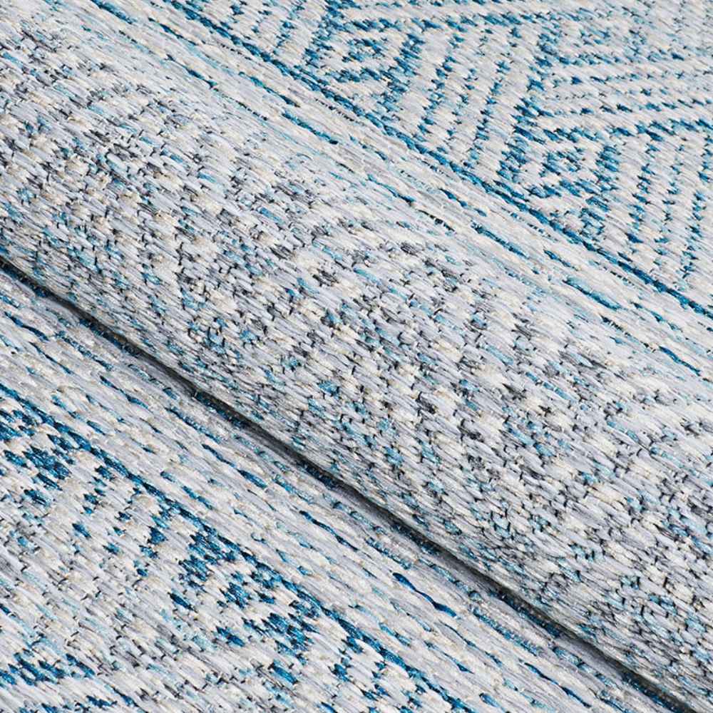 A rolled section of the Couristan Cape Indoor/Outdoor Rug - Gables/Surf highlights its thick texture and intricate diamond and zigzag patterns in surf blue and ivory