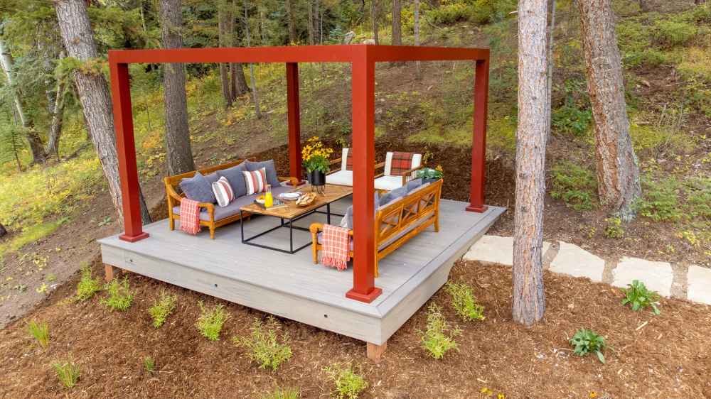As evening sets in, a white Structureworks Element Trex Pergola with soft overhead lighting creates a romantic glow on a deck overlooking the woods