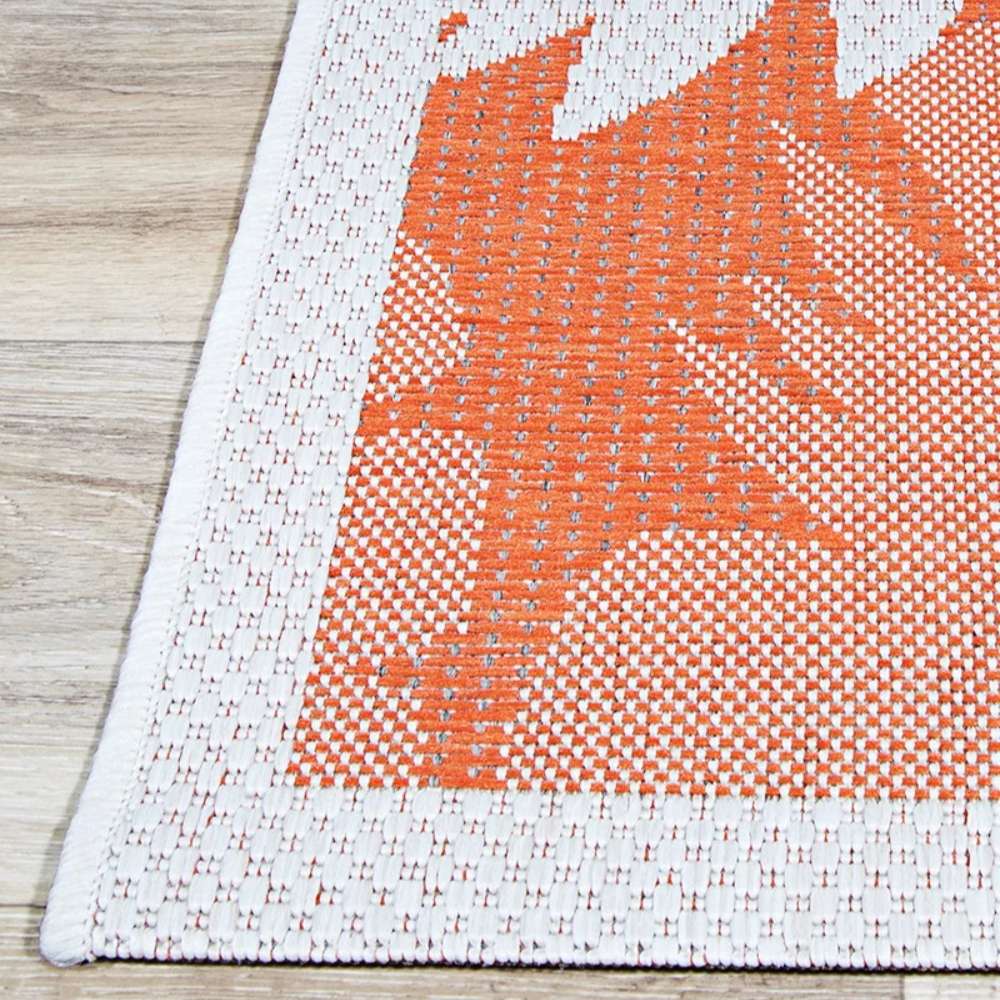 A sharp corner view of Couristan Monaco Indoor/Outdoor Rug - Coastal Flora/Ivory-Orange reveals its ivory edging and bold orange woven leaf details
