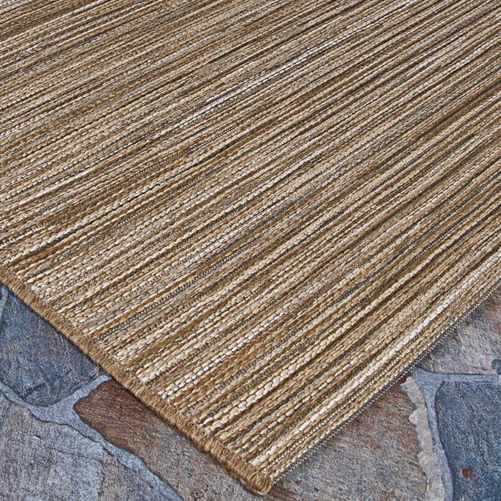 A side-angle shot displays the edge of the Couristan Cape Indoor/Outdoor Rug - Hinsdale/Brown-Ivory lying flat on an outdoor stone surface
