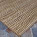 A side-angle shot displays the edge of the Couristan Cape Indoor/Outdoor Rug - Hinsdale/Brown-Ivory lying flat on an outdoor stone surface