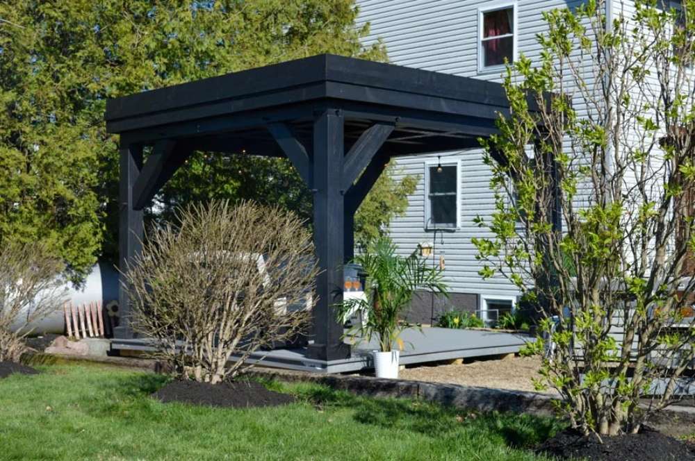 A side view of the Brookside Timber Frame Zion Resort Pergola captures its bold black design nestled in a lush backyard setting