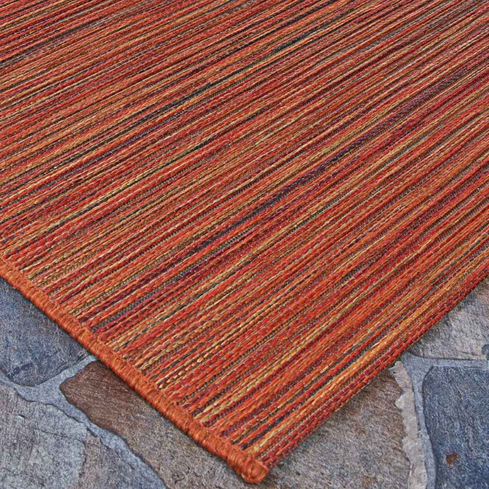 A side view of the Couristan Cape Indoor/Outdoor Rug - Hinsdale/Crimson-Multi on a stone surface reveals its thin, flat-woven texture