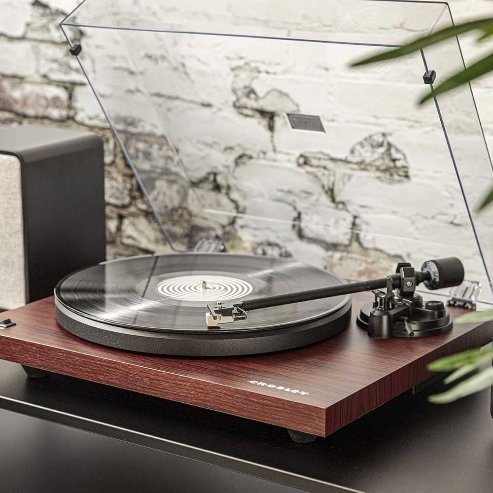 A sleek Crosley C6 Bluetooth Turntable - Mahogany with a transparent dust cover and a vinyl record playing on a modern wooden base