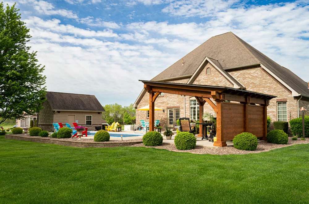 A spacious lawn with a Brookside Timber Frame Glazier Hideaway Pavilion provides a shaded retreat