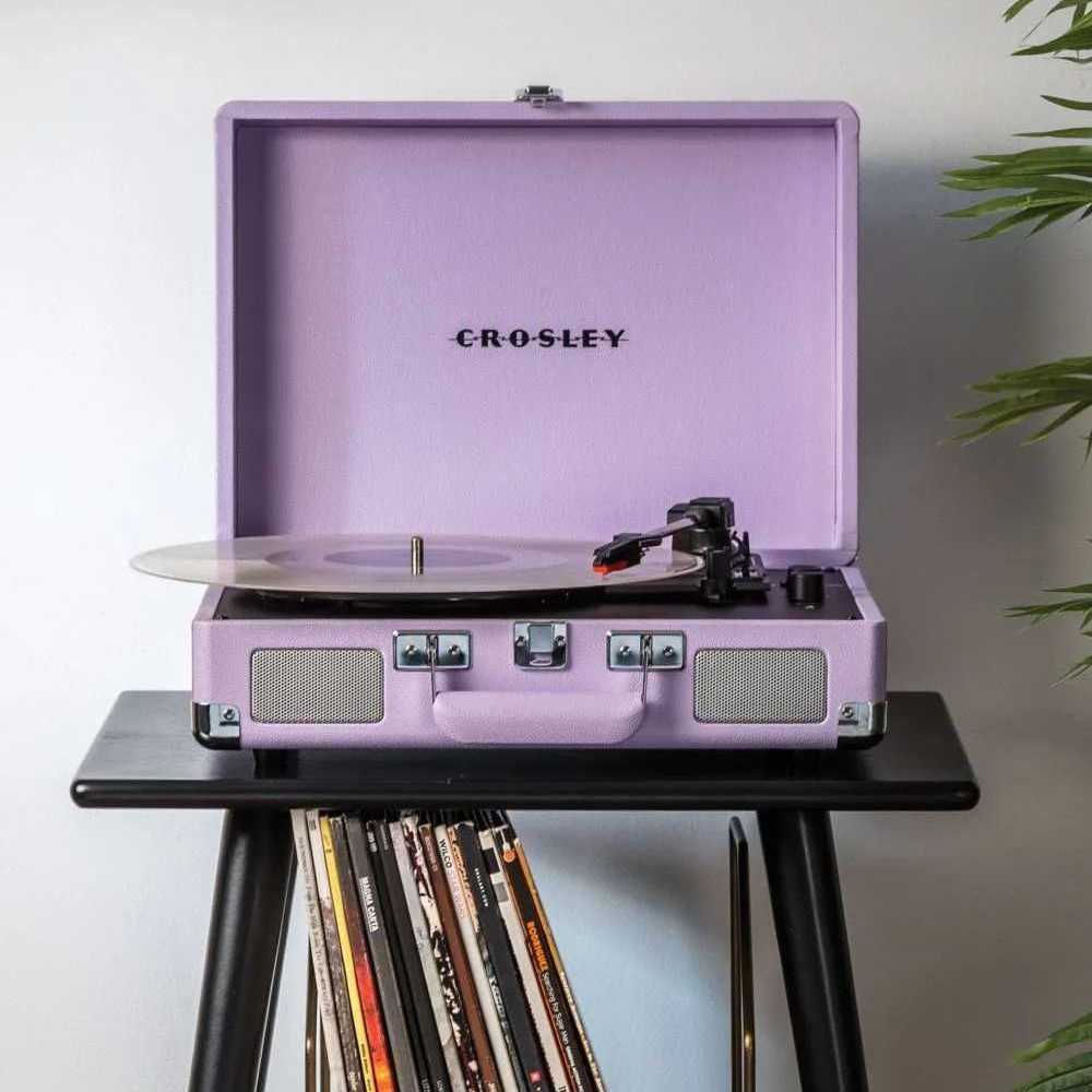 A stylish lavender Crosley Cruiser Plus Portable Turntable with Bluetooth InOut sits open on a black stand