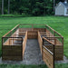 A symmetrical L-shaped layout defines the Outdoor Living Today 8×12 Raised Garden Bed, with wide gravel walkways and wooden gates for access