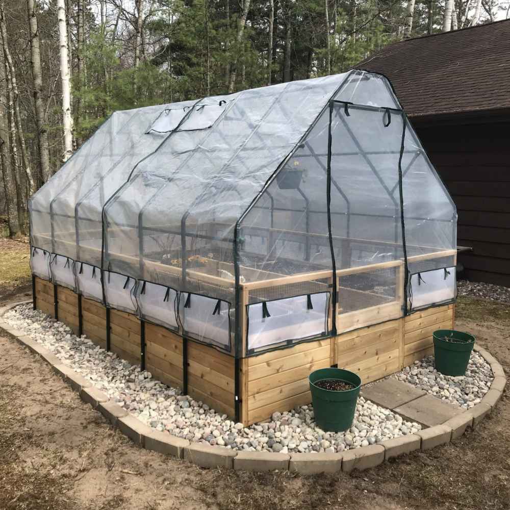 A transparent greenhouse cover is fitted over an Outdoor Living Today 8×12 Raised Garden Bed, protecting plants while letting in sunlight