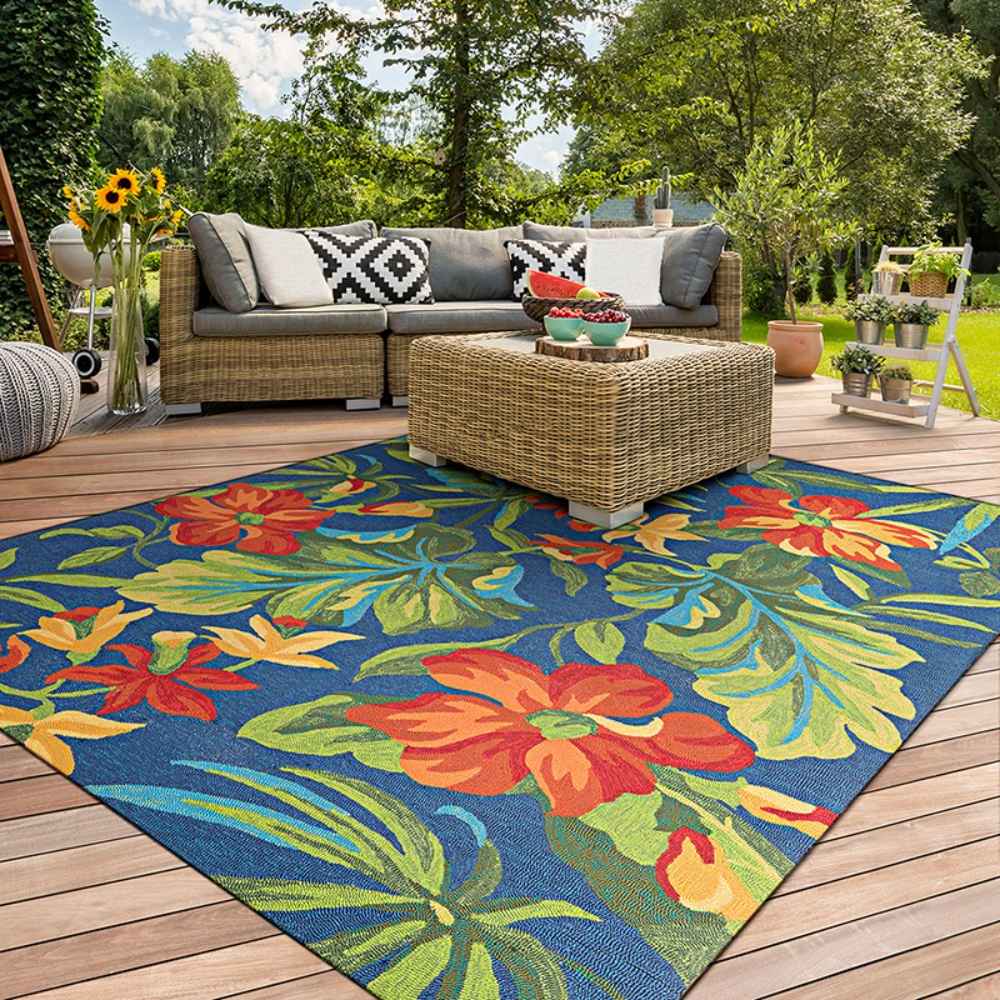 A vibrant patio scene features the Couristan Covington Indoor/Outdoor Rug - Tropical Orchid/Azure-Forest Green-Red, adding bold floral flair beneath a wicker sofa set