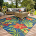A vibrant patio scene features the Couristan Covington Indoor/Outdoor Rug - Tropical Orchid/Azure-Forest Green-Red, adding bold floral flair beneath a wicker sofa set
