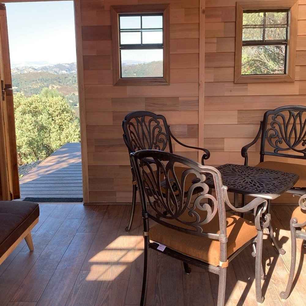 A view from inside the Outdoor Living Today 12×12 Sunshed Garden Shed shows an open door, two small windows, and a cozy setup with decorative chairs