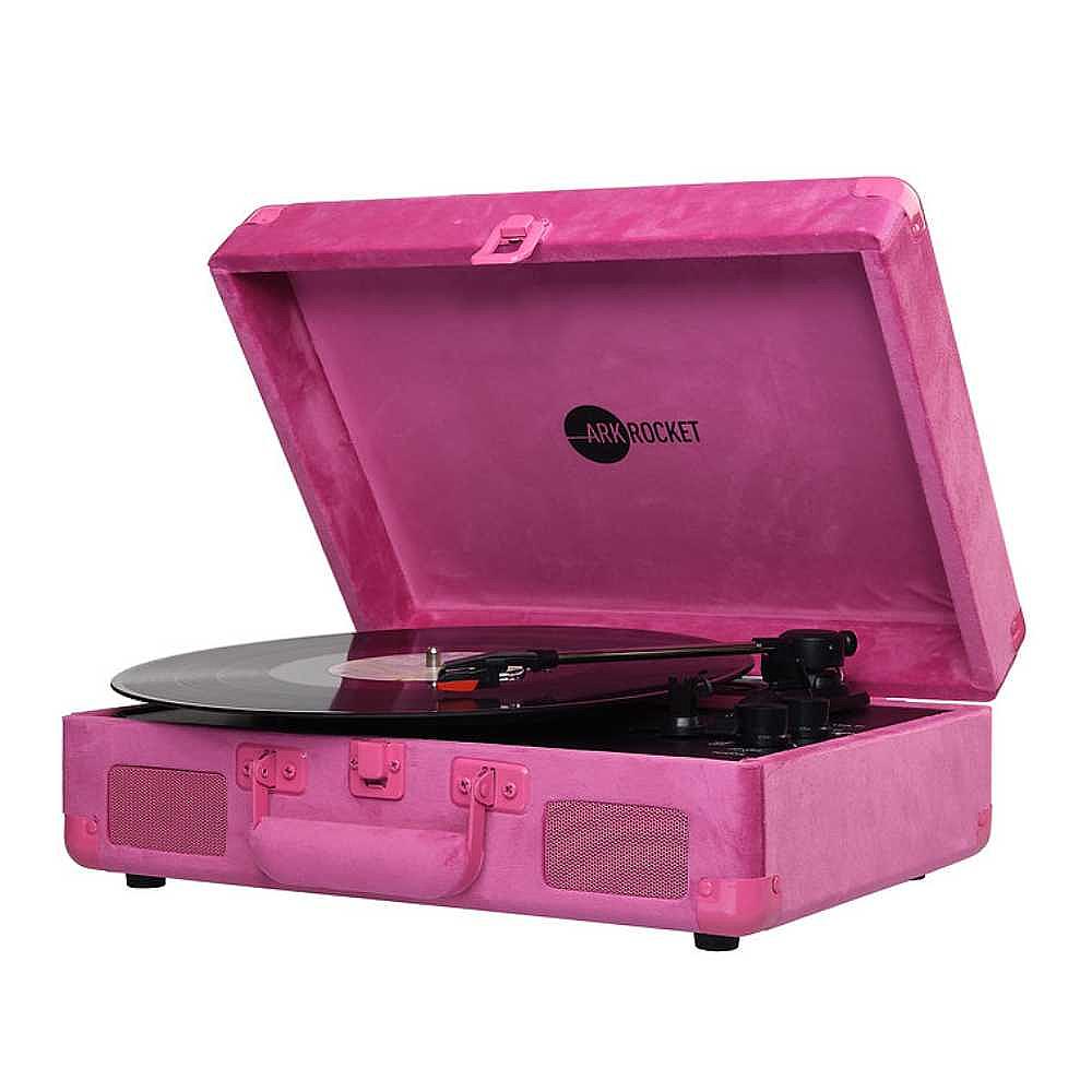 A vinyl record is playing on Arkrocket Curiosity Suitcase Bluetooth Turntable (Hot Pink Velvet) which is opened at an angle to reveal the stylus arm on the right