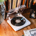 A vinyl spins on the Crosley T400D Component Bluetooth Turntable - White, surrounded by a collection of vinyl albums stored neatly on a shelf