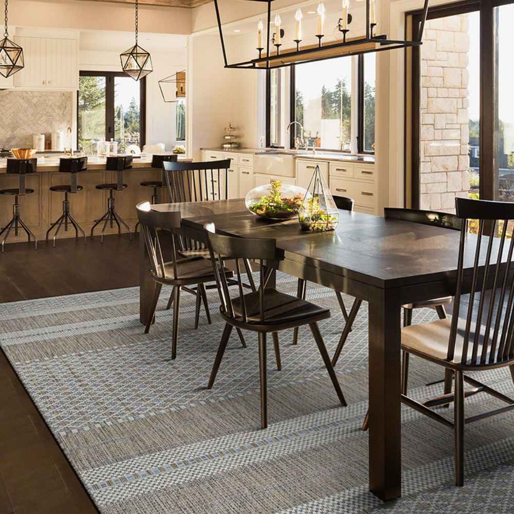 A warm, modern dining space showcases the Couristan Charm Indoor/Outdoor Rug - Yukon/Twig under a dark wooden table with high-back chairs