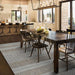 A warm, modern dining space showcases the Couristan Charm Indoor/Outdoor Rug - Yukon/Twig under a dark wooden table with high-back chairs