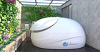 A white Dreampod Sport Float Pod is placed in a green outdoor patio with a lush vertical garden on the wall beside it