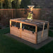 A wooden enclosure with mesh panels is bathed in evening sunlight, showing the Outdoor Living Today 6×3 Raised Garden Bed securely set up on a patch of soil